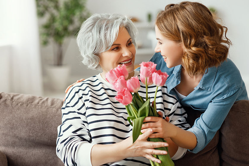 Cheerful young female hugging happy aged mother giving bouquet tulips Cheerful young female hugging happy aged mother giving bouquet tulips