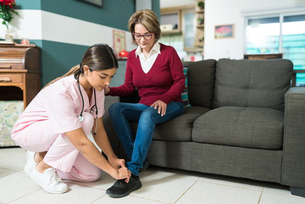 female nurse tying shoelace senior woman sitting sofa