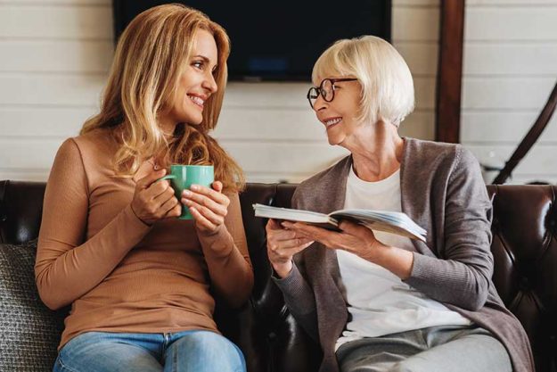 mature women reading book her daughter drinking coffee home mature women reading book her daughter drinking coffee home