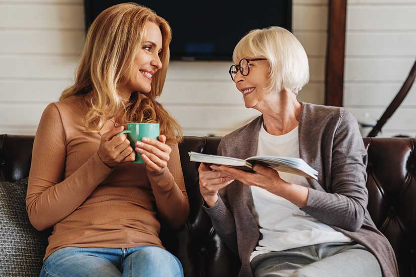 mature women reading book her daughter drinking coffee home