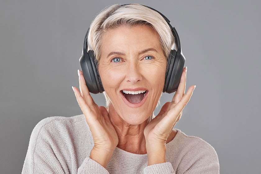 One happy mature woman isolated grey background studio wearing headphones One happy mature woman isolated grey background studio wearing headphones