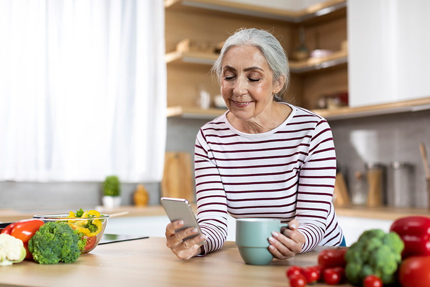 portrait smiling senior woman using smartphone drinking coffee