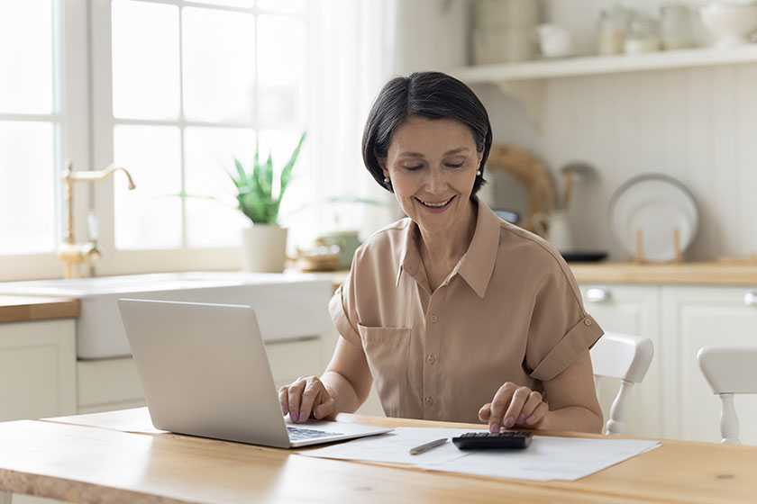 Positive satisfied mature homeowner woman counting money calculator using laptop