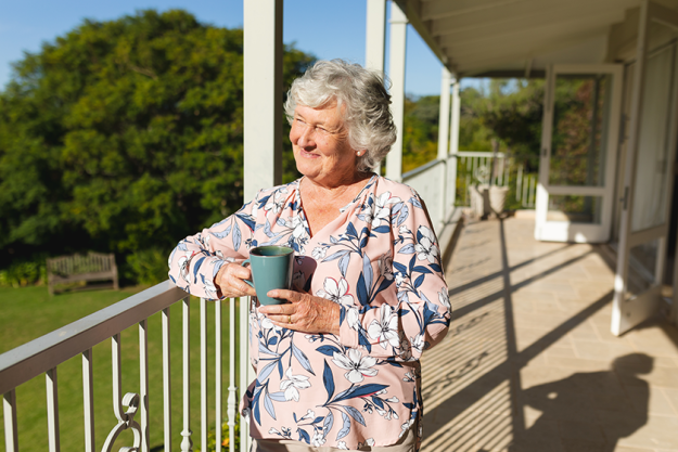 senior caucasian woman standing balcony holding mug