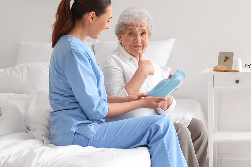 Young caregiver hot water bottle senior woman bedroom