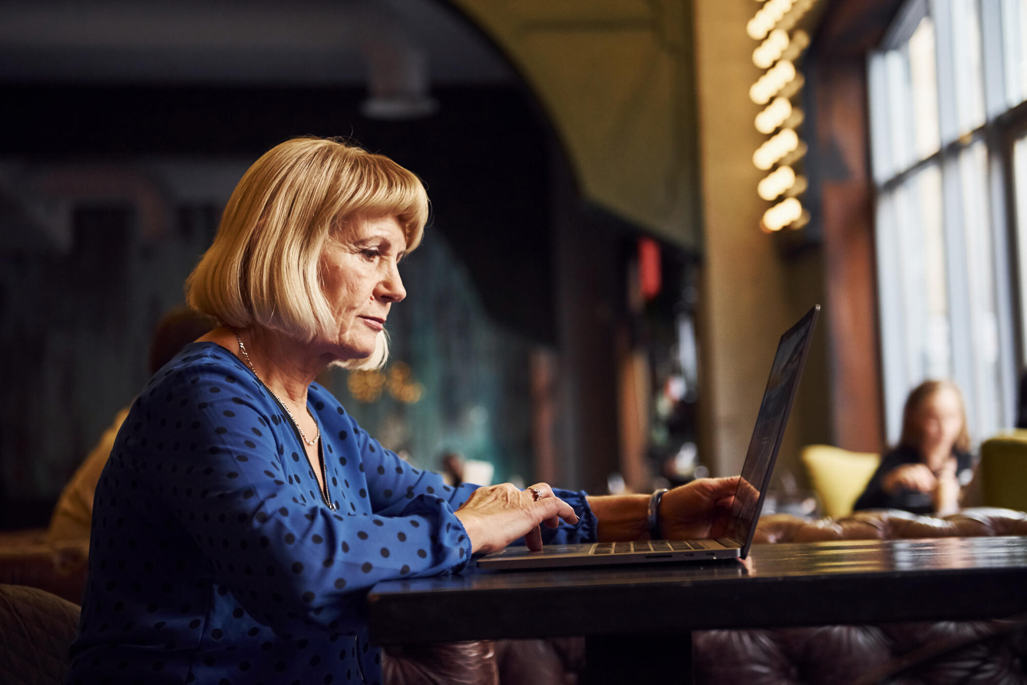 Portrait of senior woman that sits indoors in the cafe with modern laptop