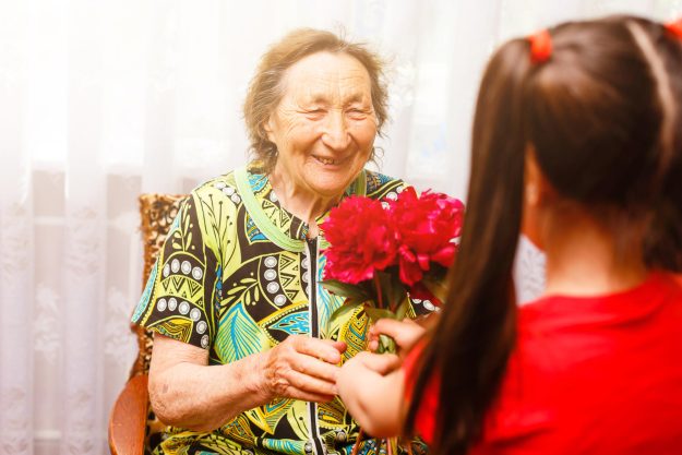 little girl giving her great grandmother a pink flower