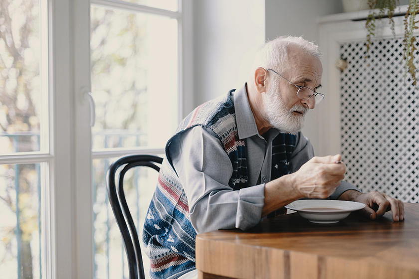 senior grandfather grey hair beard sitting alone kitchen eating breakfast