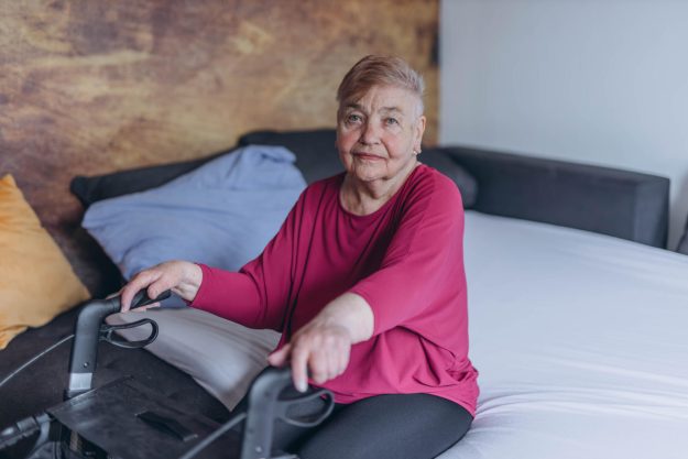 A lonely grandmother sits on her bed and looks out the window. Walkers for the elderly A lonely grandmother sits on her bed and looks out the window. Walkers for the elderly