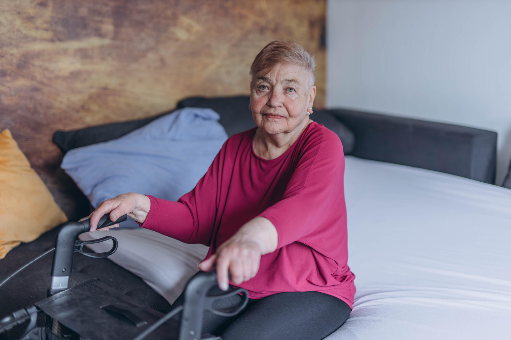 A lonely grandmother sits on her bed and looks out the window. Walkers for the elderly A lonely grandmother sits on her bed and looks out the window. Walkers for the elderly