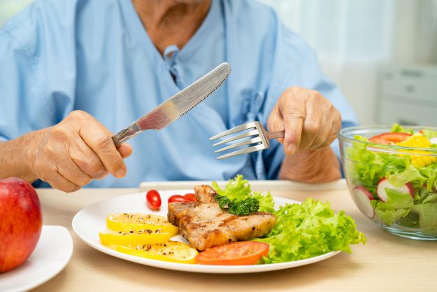 Asian elderly woman patient eating salmon stake and vegetable sa Asian elderly woman patient eating salmon stake and vegetable sa