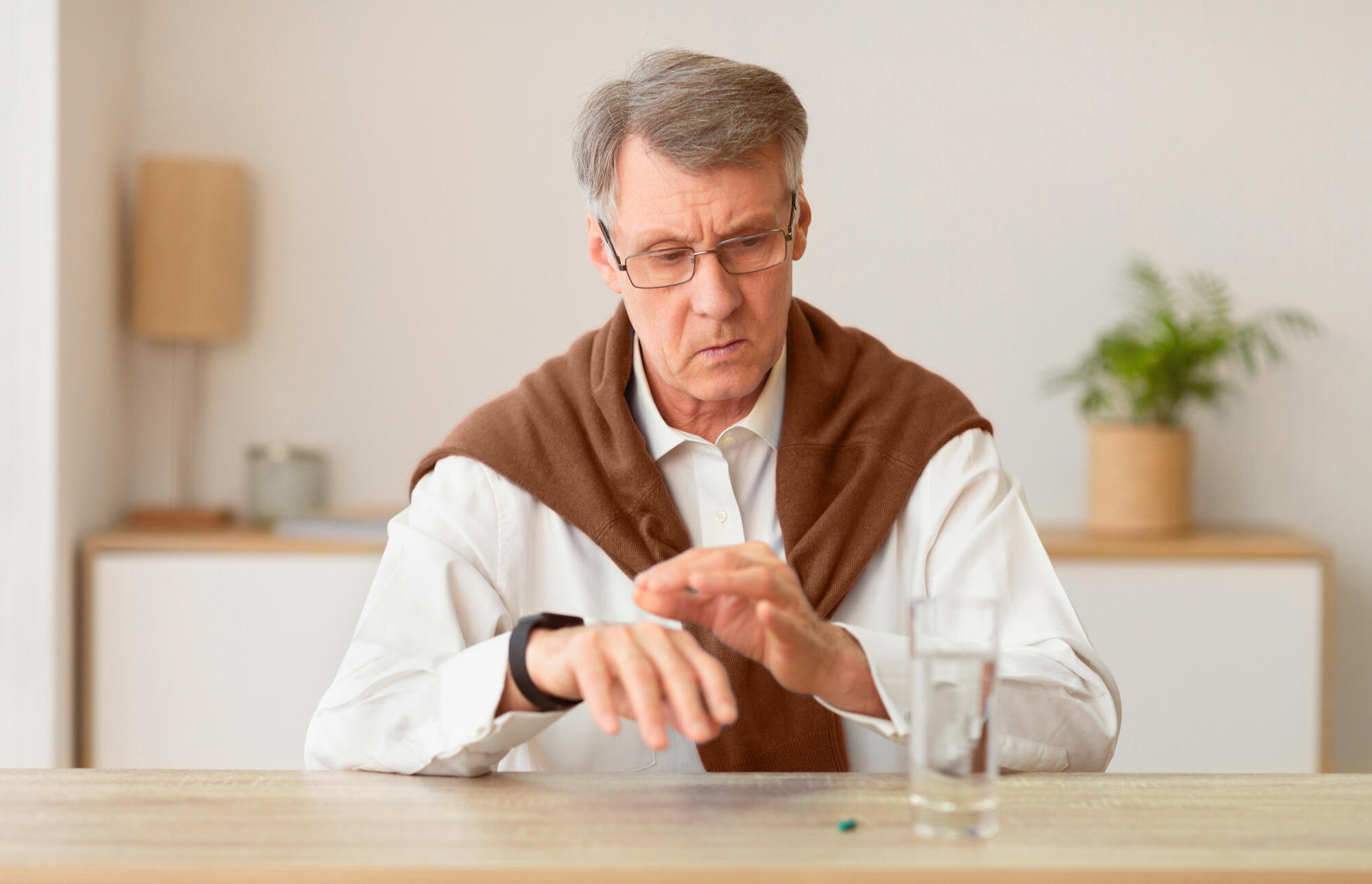 Gentleman Checking Smartwatch Sitting At Table With Pill And Water Gentleman Checking Smartwatch Sitting At Table With Pill And Water