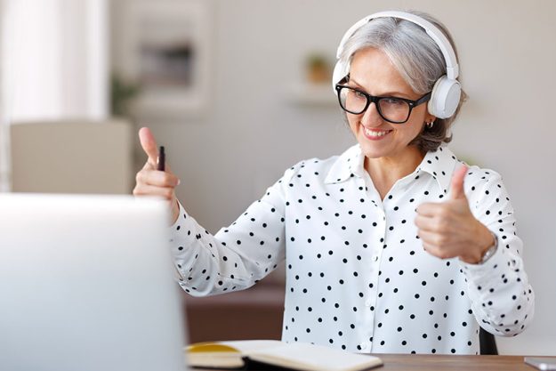 Beautiful smiling mature woman in headphones during online meeting on laptop with collegues at home Beautiful smiling mature woman in headphones during online meeting on laptop with collegues at home