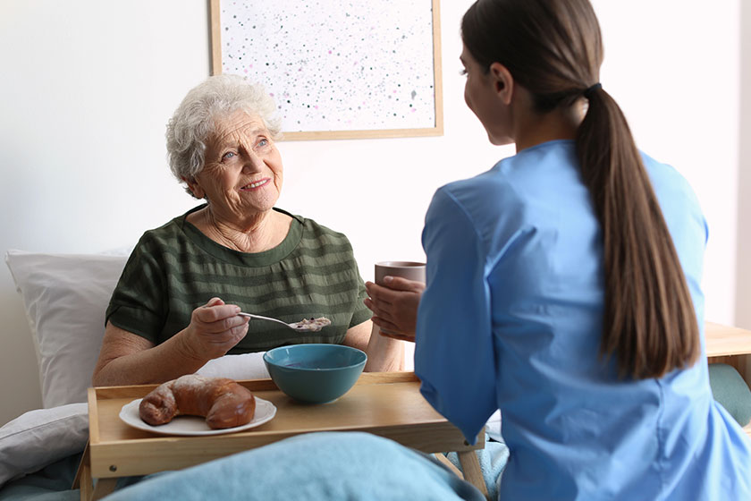 Care worker serving dinner for elderly woman in geriatric hospic