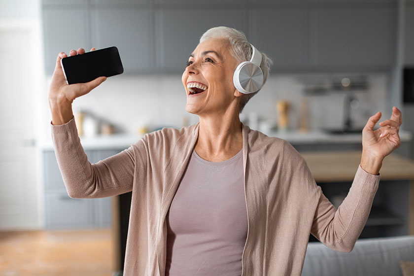 Cheerful european senior lady smartphone headphones singing song having fun Cheerful european senior lady smartphone headphones singing song having fun