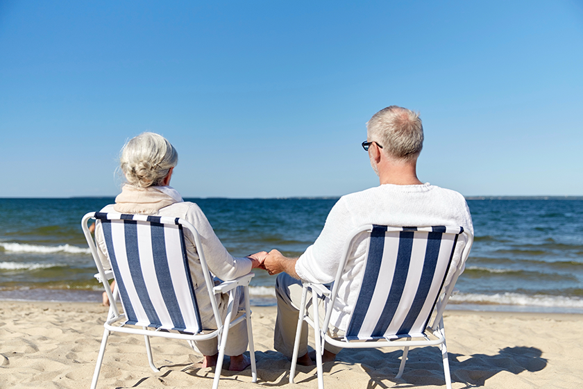 senior couple sitting on chairs at summer beach