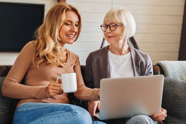 Happy mature woman her adult daughter smiling while sitting sofa Happy mature woman her adult daughter smiling while sitting sofa