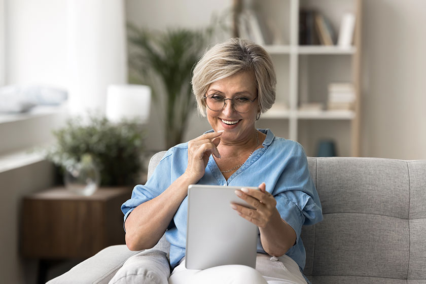 Smiling mature woman sit comfortably sofa tablet read social media