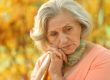 Portrait of beautiful sad senior woman on blurred autumn background