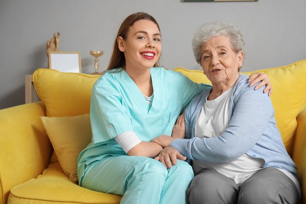 Female caregiver senior woman sitting sofa home