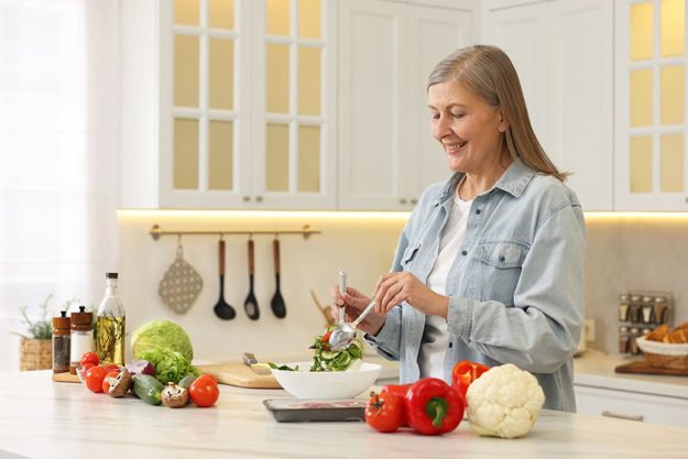 Happy woman making salad table kitchen
