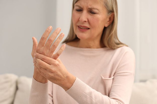 Mature woman suffering pain hand indoors selective focus rheumatism symptom Mature woman suffering pain hand indoors selective focus rheumatism symptom