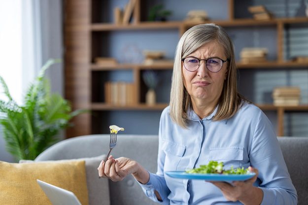 Senior woman glasses holds plate salad showing dissatisfaction healthy food