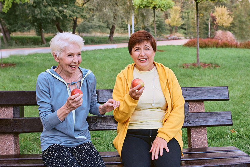 Two mature women eating apples bench doing sport exercises park Two mature women eating apples bench doing sport exercises park