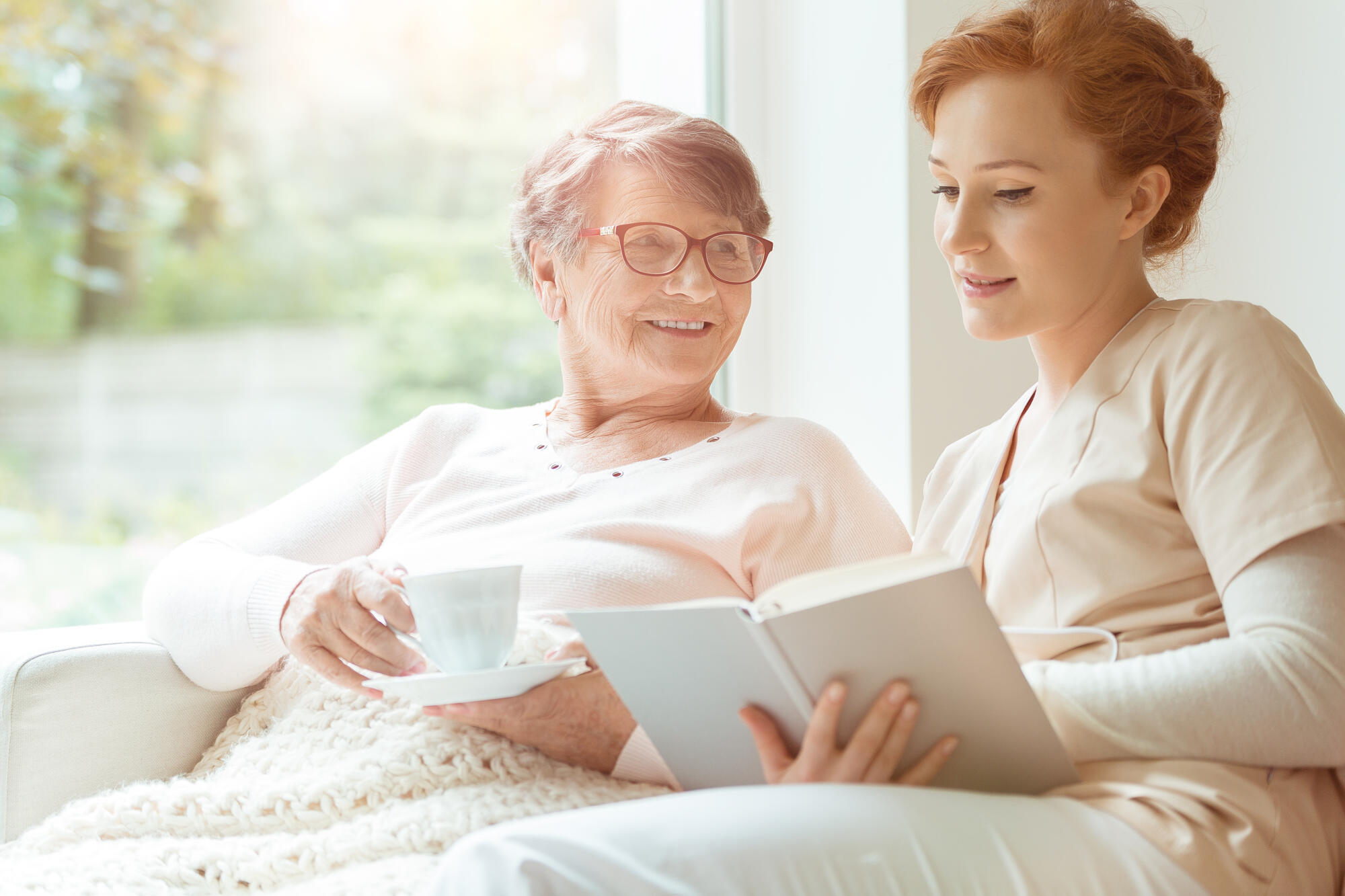 Woman,Reading,A,Book,While,Sitting,With,Happy,Grandmother,Drinking