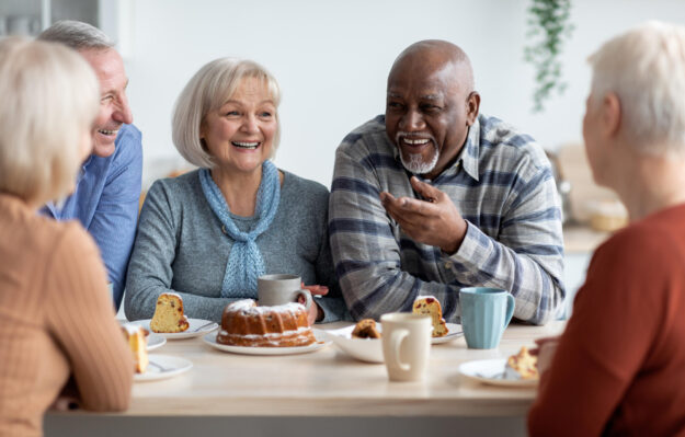 International group of positive elderly people drinking tea with cake
