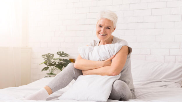 Senior woman hugging white pillow at home