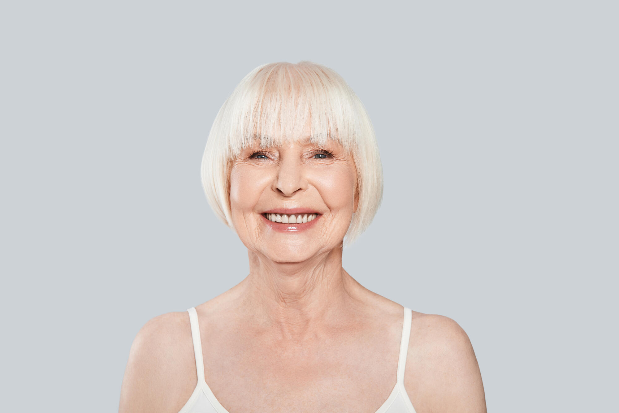 Enjoying life. Beautiful senior woman looking at camera and smiling while standing against grey background