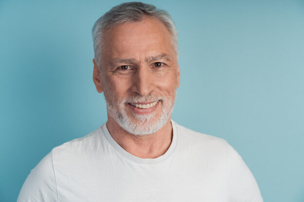 Close up view, senior, attractive man smiling, looking straight into the camera. Handsome man with gray beard isolated on blue background. Close up view, senior, attractive man smiling, looking straight into the camera. Handsome man with gray beard isolated on blue background.