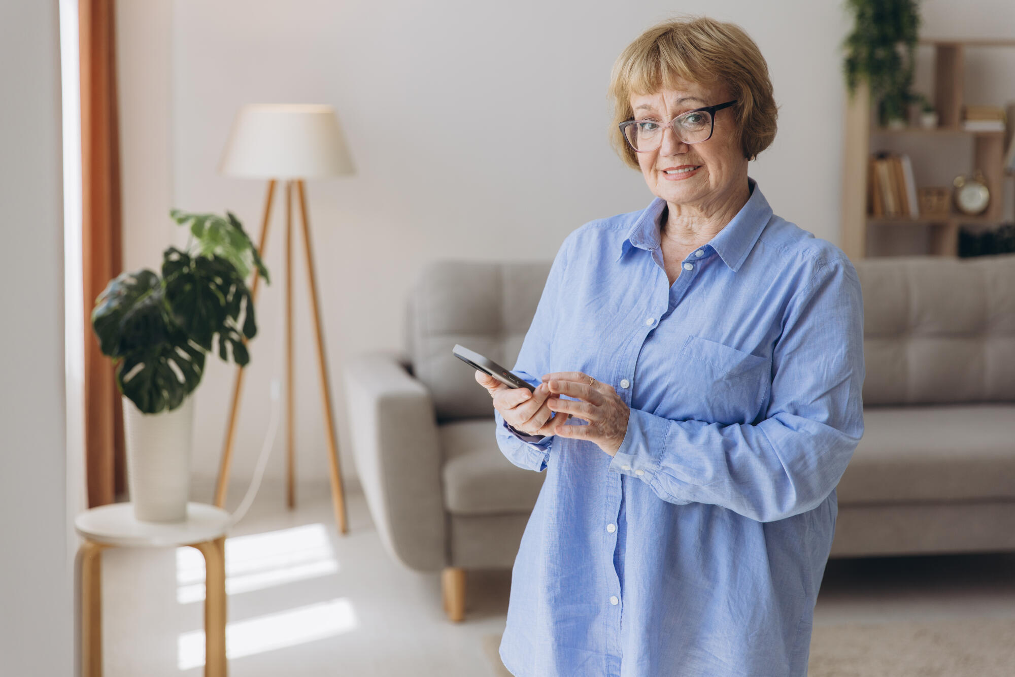 Senior woman stand at the window at home use mobile phone smartp