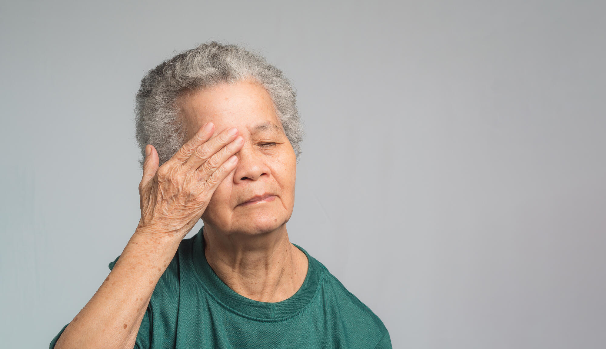Portrait of a senior woman with eye pain while standing on a gra