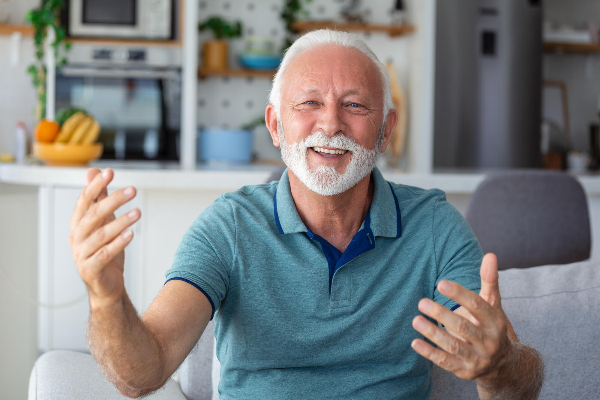Smiling senior man wave to camera having video call on laptop, happy elderly male sit on couch at home talk using modern technologies and wireless connection