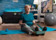 Retirement senior woman sitting on yoga mat stretching legs muscles using stretch elastic band