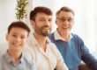 Senior Man, Son And Grandson Sitting On Sofa At Home