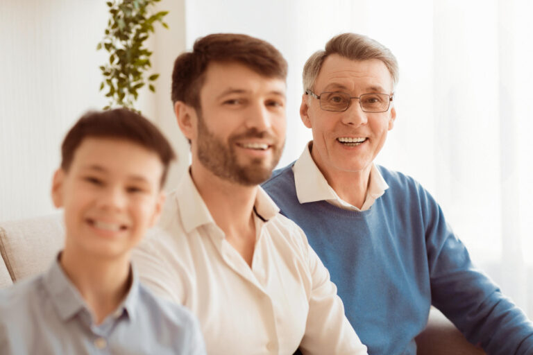 Senior Man, Son And Grandson Sitting On Sofa At Home Senior Man, Son And Grandson Sitting On Sofa At Home