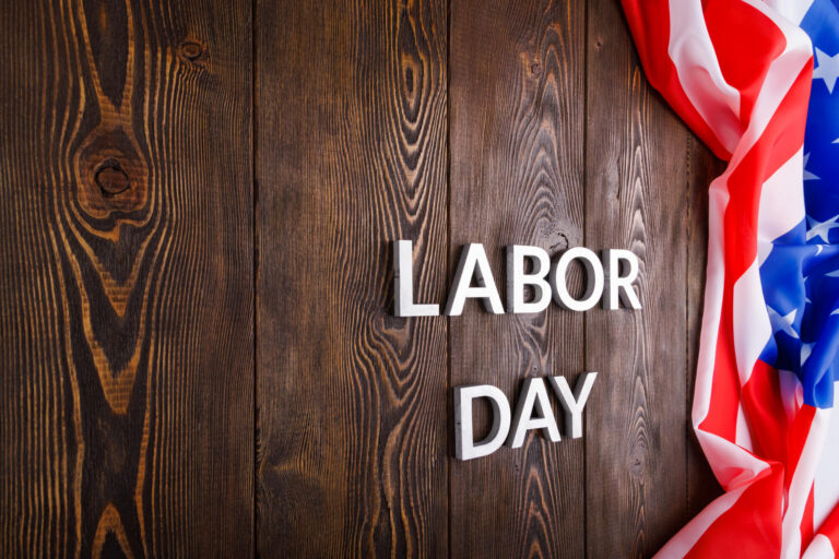 words labor day laid with silver metal letters on wooden surface with crumpled USA flag on left side