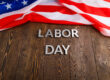 words labor day laid with silver metal letters on wooden surface with crumpled USA flag on left side