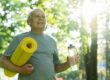 Active elderly man with a exercise mat and bottle of water in green city park