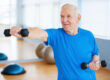 Struggling with age. Confident senior man exercising with dumbbells and smiling while standing in health club