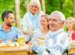 Enjoying time with family. Happy family of five people sitting at the dining table outdoors while senior man looking over shoulder and smiling