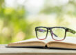 Book and eye glasses on wooden table with abstract green nature