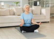 Yoga mindfulness meditation. Senior adult mature woman practicing yoga at home. Mid age old lady sitting in lotus pose on yoga mat meditating relaxing, Older middle aged woman doing breathing practice