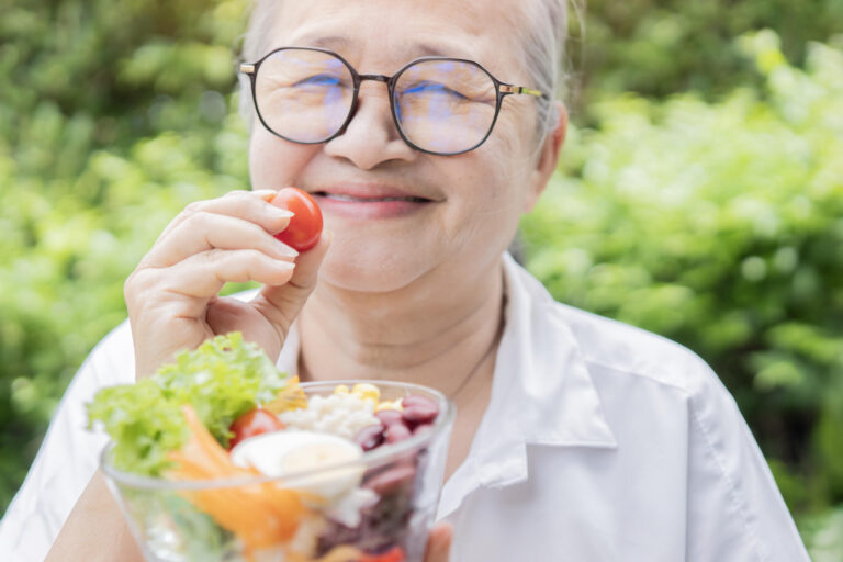 Happy Asian retirement women holding a tomato with fresh salad b