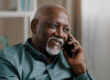 African middle aged business man senior mature businessman entrepreneur at home in office talking phone chatting mobile conversation booking order with smartphone call discussing remote talk speaking