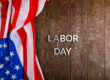 words labor day laid with silver metal letters on wooden surface with crumpled USA flag on left side