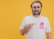 Senior Man Showing Pink Ribbon for Breast Cancer Awareness on Yellow Background